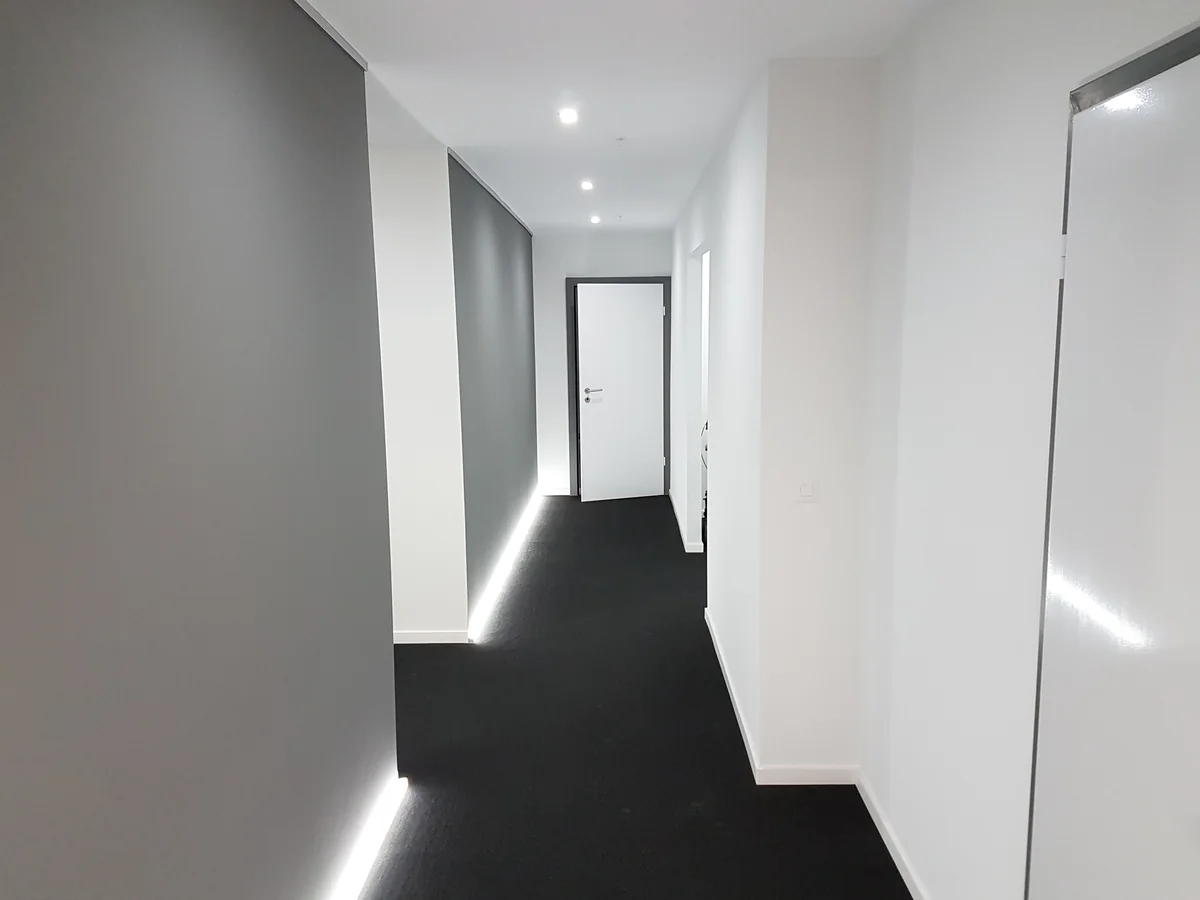 Couloir aux murs blancs et gris avec éclairage au pied du mur
